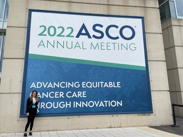 A female member of the BCD Meetings & Events 'event team' standing in front of a large ASCO banner | Global Agency. BCD Meetings & Events