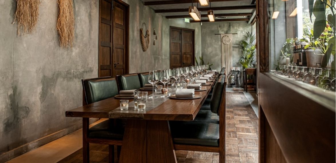 Long wooden table with leather chairs and laid up. Concrete style walls
